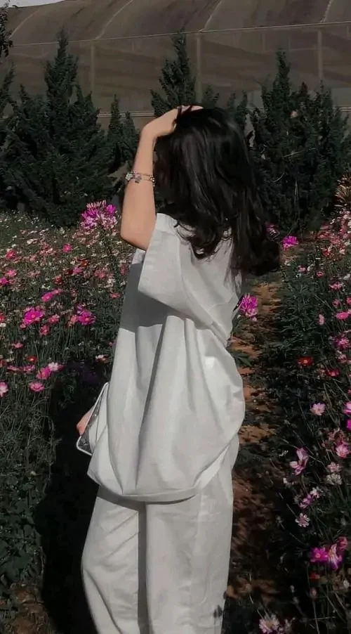 Giữa vườn hoa hồng, hình gái đẹp giấu kín diện mạo nghiêng người chạm tóc, váy trắng ôm nhẹ và mái tóc đen phủ vai