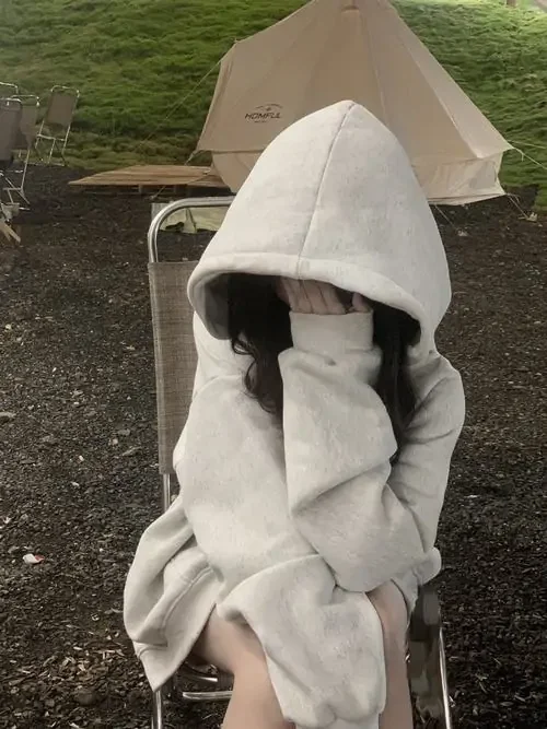 Gái xinh che mặt trong áo hoodie trắng ngồi giữa lều ngoài trời, hai tay kéo mũ thấp, dáng co người nhỏ nhắn và kín đáo