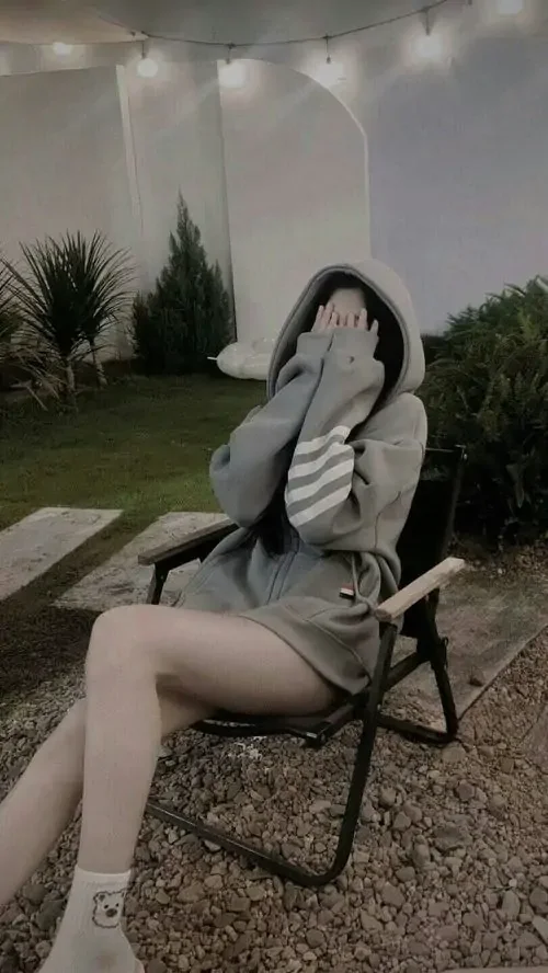 Bên chiếc ghế nhỏ ngoài sân, ảnh gái xinh phong cách bí ẩn hiện lên qua hoodie rộng, khẩu trang trắng và dáng ngồi nghiêng lặng lẽ