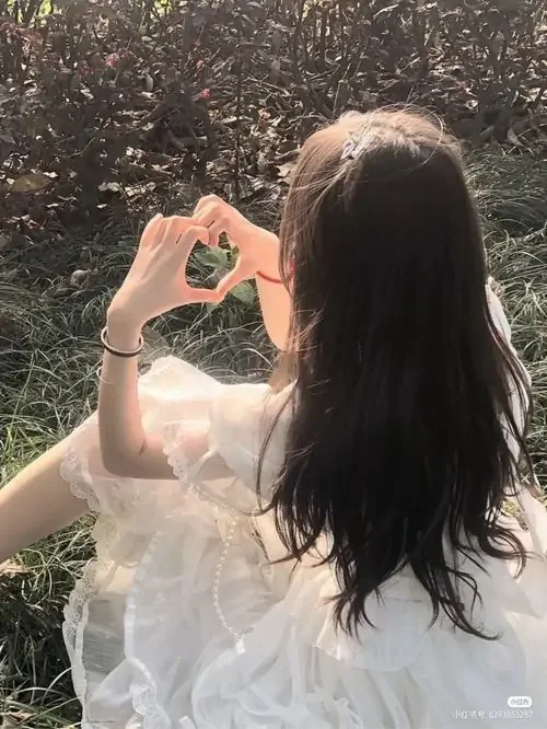 Nắng chiều xuyên qua tóc dài, cô gái đưa tay tạo hình trái tim trước mặt, váy trắng mỏng nhẹ làm khung hình dịu và ấm