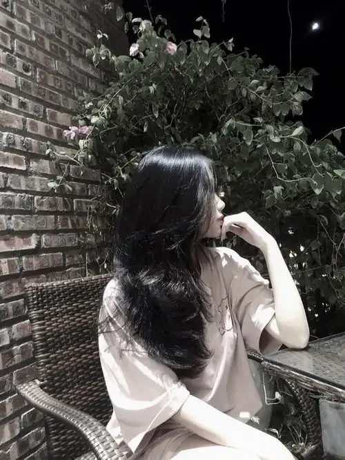 Góc nghiêng bên tường gạch làm ảnh hot girl giấu mặt nghệ thuật mềm hơn, áo trắng lệch vai và tóc xoăn đen tạo điểm nhấn